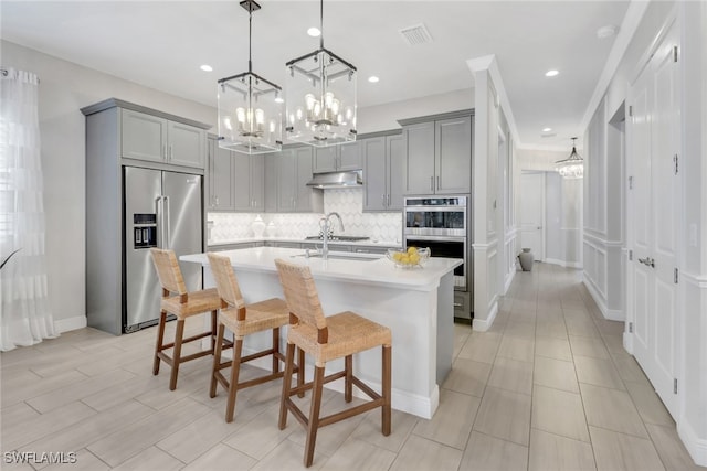 kitchen featuring stainless steel appliances, a kitchen island with sink, a breakfast bar area, and gray cabinetry