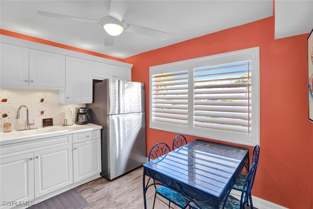 kitchen with white cabinets, sink, decorative backsplash, light wood-type flooring, and stainless steel refrigerator