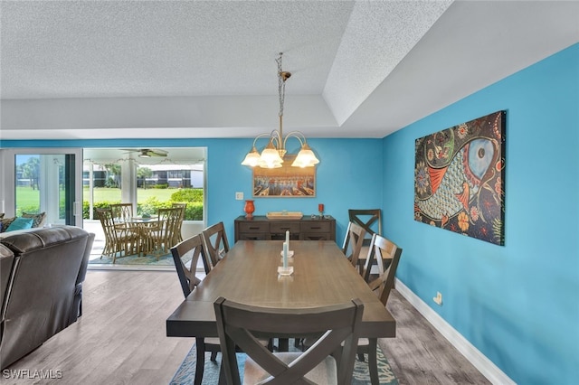 dining area with ceiling fan with notable chandelier, wood-type flooring, a textured ceiling, and a tray ceiling