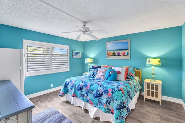 bedroom with hardwood / wood-style floors, ceiling fan, white fridge, and a textured ceiling