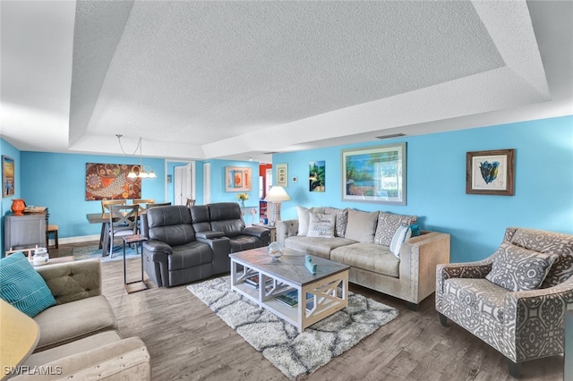 living room with wood-type flooring, a textured ceiling, a tray ceiling, and a notable chandelier