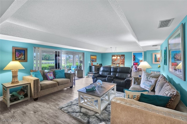 living room featuring a textured ceiling, hardwood / wood-style flooring, a raised ceiling, and a notable chandelier