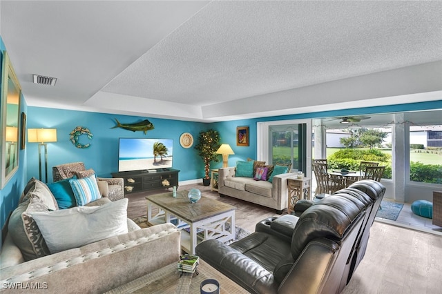 living room with ceiling fan, a textured ceiling, and light hardwood / wood-style flooring