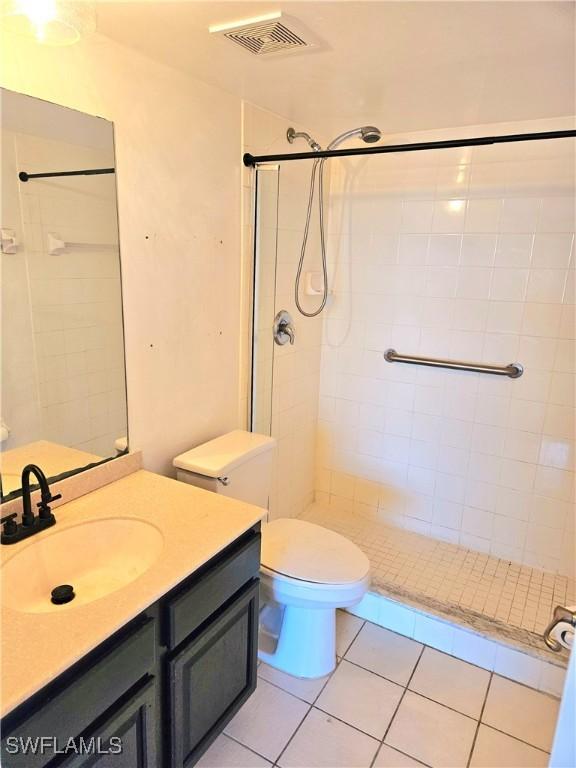 bathroom with tile patterned floors, vanity, a tile shower, and toilet