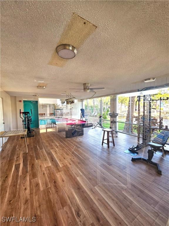 workout area with ceiling fan, wood-type flooring, and a textured ceiling