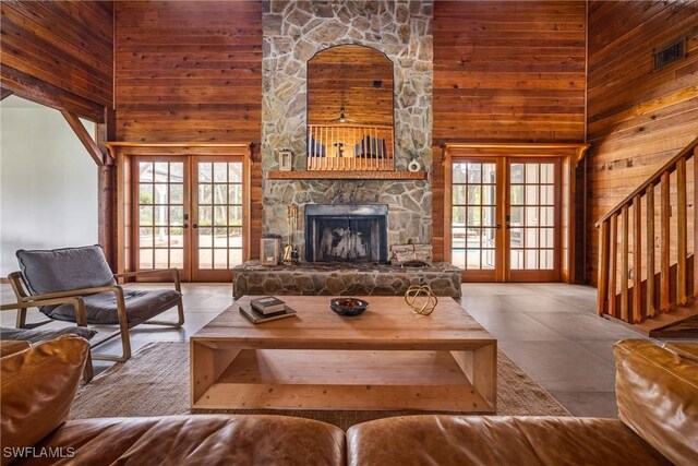 living room featuring french doors, high vaulted ceiling, wooden walls, and a stone fireplace