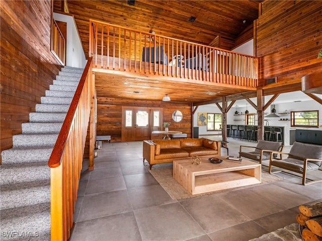 living area with wooden ceiling, wood walls, stairway, and a high ceiling