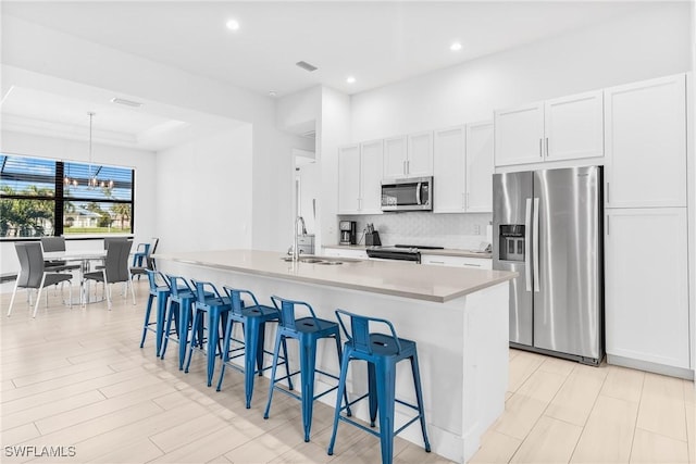 kitchen with sink, stainless steel appliances, a kitchen island with sink, a breakfast bar, and white cabinets