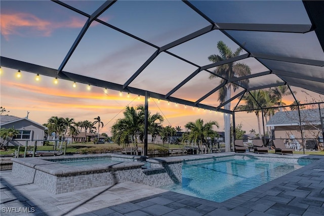 pool at dusk with glass enclosure, a patio area, and an in ground hot tub