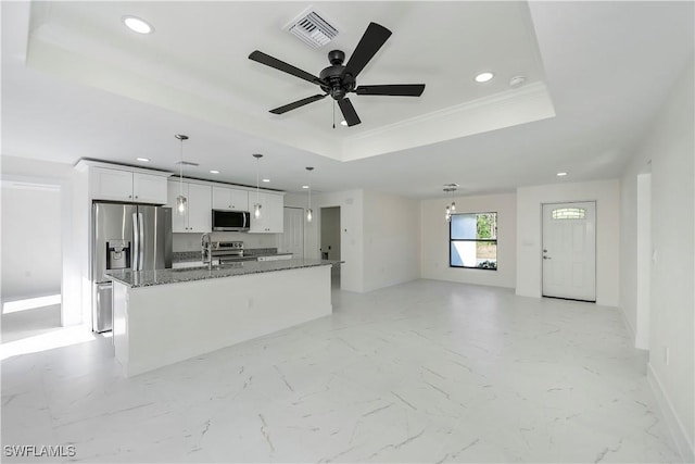 kitchen featuring white cabinetry, a raised ceiling, dark stone counters, a center island with sink, and appliances with stainless steel finishes