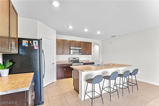 kitchen with a center island with sink, sink, light tile patterned floors, appliances with stainless steel finishes, and a breakfast bar area