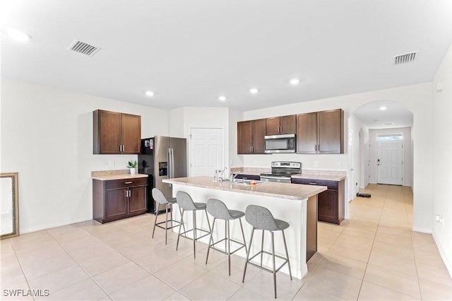 kitchen with a center island with sink, a kitchen bar, light tile patterned floors, and appliances with stainless steel finishes