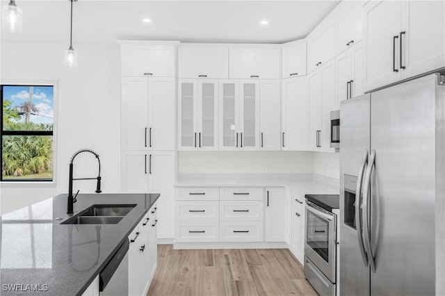 kitchen featuring light wood-type flooring, stainless steel appliances, sink, white cabinetry, and hanging light fixtures