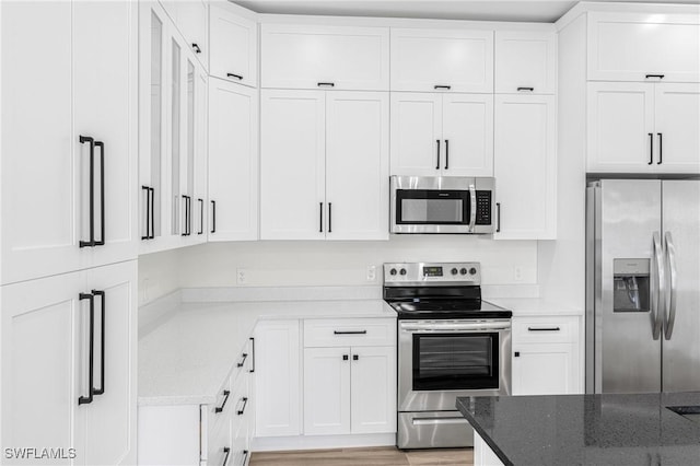 kitchen with dark stone countertops, white cabinetry, light hardwood / wood-style flooring, and appliances with stainless steel finishes