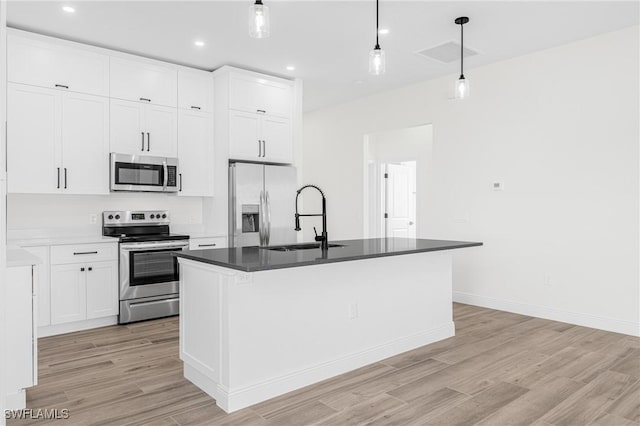 kitchen featuring white cabinetry, stainless steel appliances, light hardwood / wood-style floors, decorative light fixtures, and a center island with sink