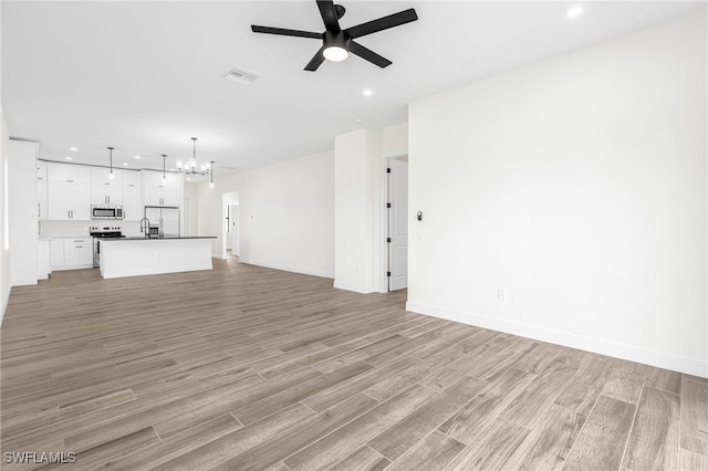 unfurnished living room with ceiling fan with notable chandelier, light wood-type flooring, and sink