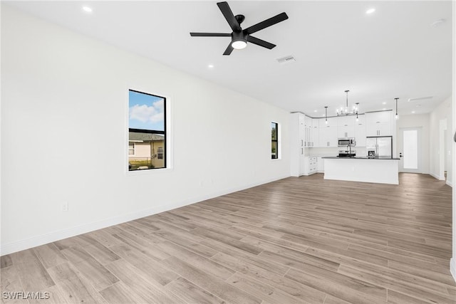 unfurnished living room featuring ceiling fan with notable chandelier and light wood-type flooring