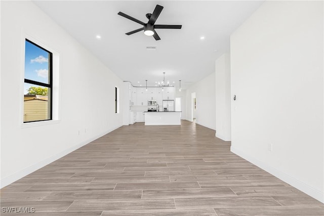 unfurnished living room featuring ceiling fan with notable chandelier and light hardwood / wood-style flooring