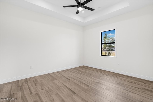 spare room featuring ceiling fan, light hardwood / wood-style floors, and a raised ceiling