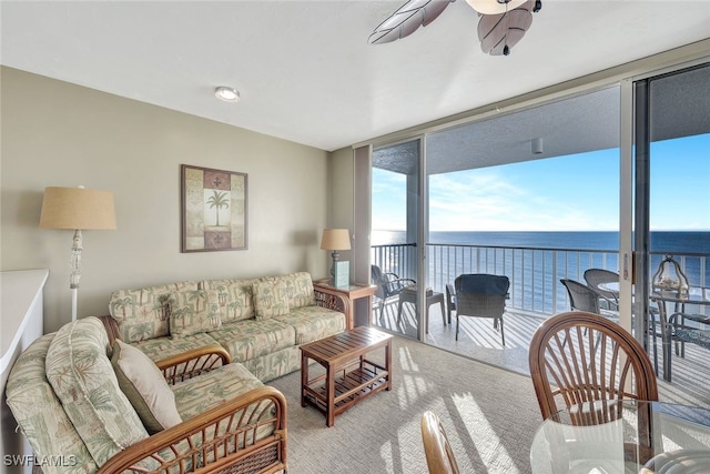 carpeted living room with expansive windows, ceiling fan, and a water view