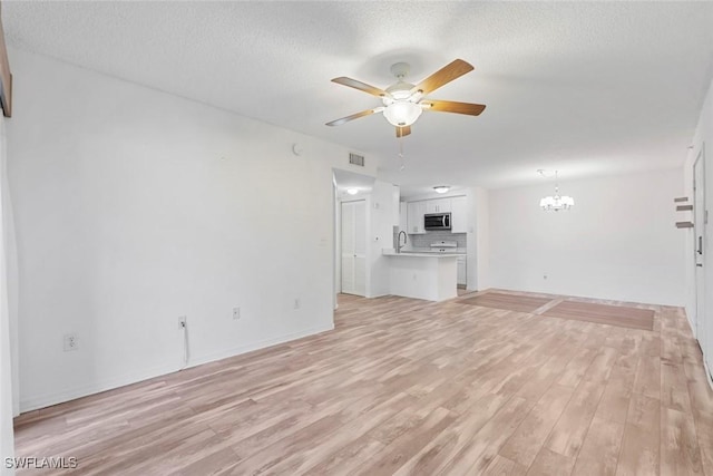 unfurnished living room featuring ceiling fan with notable chandelier, a textured ceiling, light hardwood / wood-style flooring, and sink