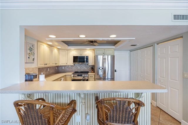 kitchen featuring a raised ceiling, light tile patterned floors, a kitchen bar, kitchen peninsula, and stainless steel appliances