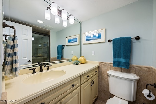 bathroom with vanity, a shower with shower door, tile walls, and toilet