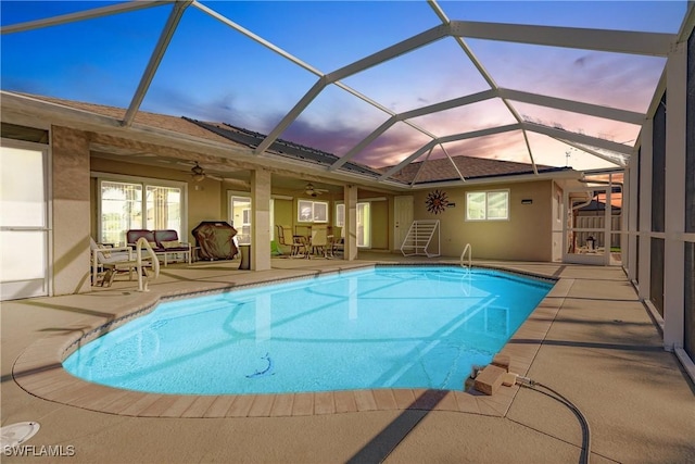 pool at dusk featuring a lanai, a patio area, and ceiling fan