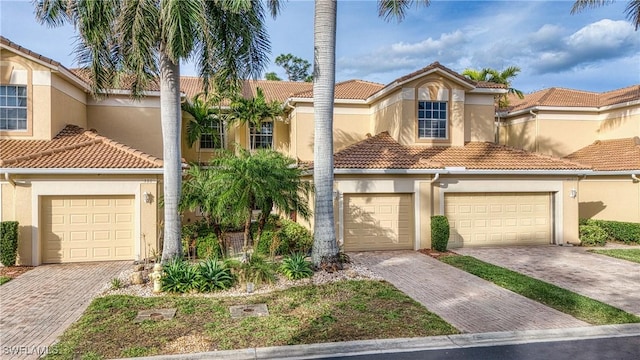 mediterranean / spanish-style house featuring a garage, a tile roof, decorative driveway, and stucco siding