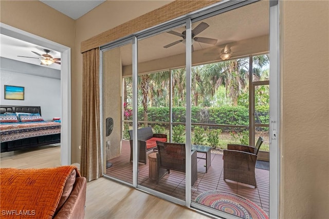 doorway to outside featuring light wood-type flooring, a sunroom, a textured wall, and ceiling fan