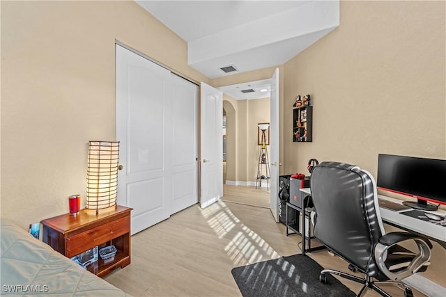 office featuring arched walkways, visible vents, light wood-style flooring, and baseboards