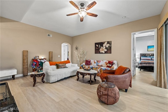 living area with light wood-type flooring, visible vents, arched walkways, and a ceiling fan