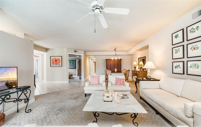 carpeted living area with ceiling fan with notable chandelier, visible vents, baseboards, and tile patterned floors