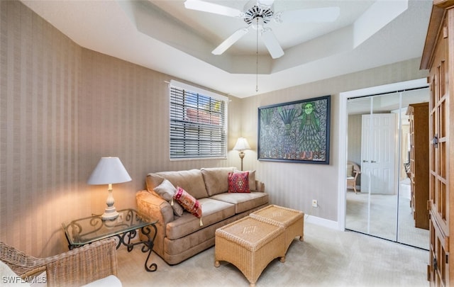 living room featuring ceiling fan, light carpet, baseboards, a tray ceiling, and wallpapered walls