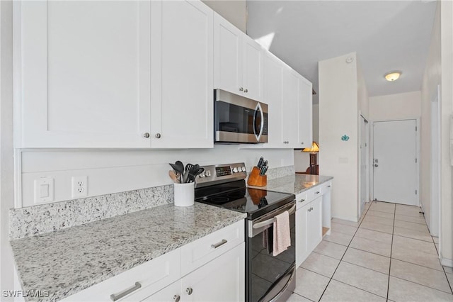 kitchen with white cabinets, light tile patterned floors, stainless steel appliances, and light stone counters