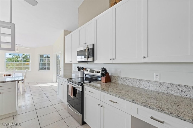 kitchen with white cabinets, light stone counters, light tile patterned floors, and stainless steel appliances