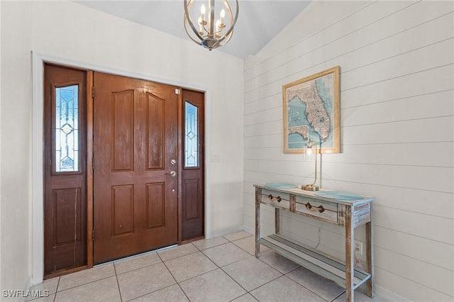 entryway featuring wooden walls, light tile patterned flooring, vaulted ceiling, and a notable chandelier