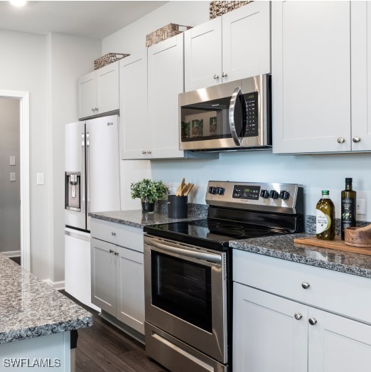 kitchen featuring dark stone countertops, white cabinetry, dark wood-type flooring, and appliances with stainless steel finishes