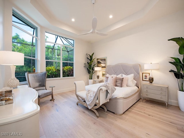 bedroom featuring multiple windows, light wood-type flooring, ceiling fan, and a tray ceiling