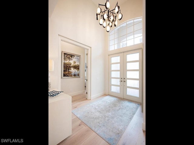 entrance foyer with french doors, a chandelier, a high ceiling, and light wood-type flooring