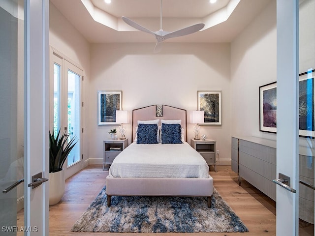 bedroom featuring light hardwood / wood-style floors, access to outside, ceiling fan, and a tray ceiling