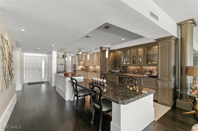 bar featuring decorative backsplash, dark stone counters, sink, wood-type flooring, and hanging light fixtures