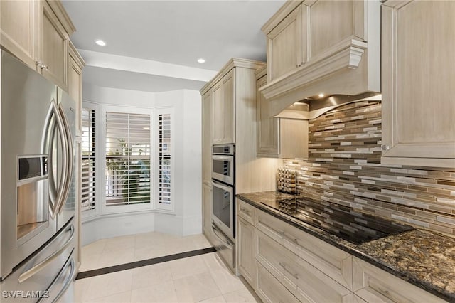 kitchen with decorative backsplash, stainless steel appliances, light brown cabinets, dark stone countertops, and light tile patterned flooring