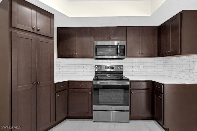 kitchen with tasteful backsplash, dark brown cabinetry, light stone countertops, and appliances with stainless steel finishes