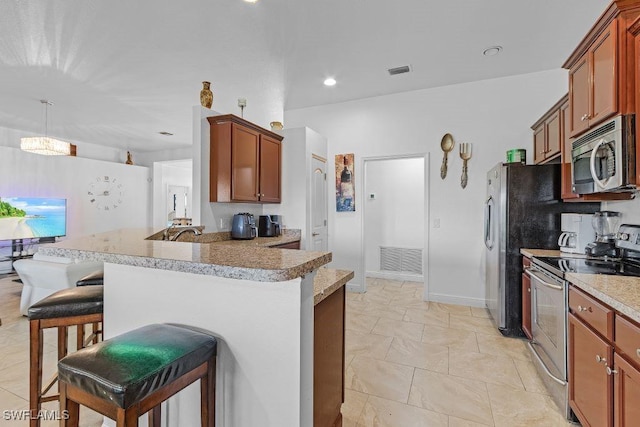 kitchen with a kitchen bar, appliances with stainless steel finishes, kitchen peninsula, and decorative light fixtures