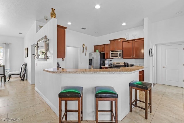 kitchen featuring a kitchen breakfast bar, light tile patterned floors, light stone counters, kitchen peninsula, and stainless steel appliances