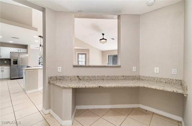 kitchen with light stone countertops, tasteful backsplash, kitchen peninsula, stainless steel fridge, and white cabinets