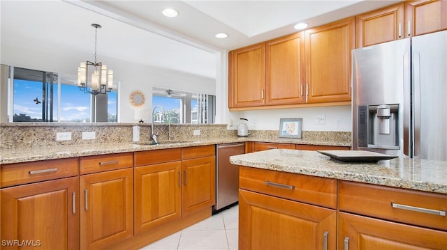 kitchen featuring light stone countertops, stainless steel appliances, sink, light tile patterned floors, and hanging light fixtures