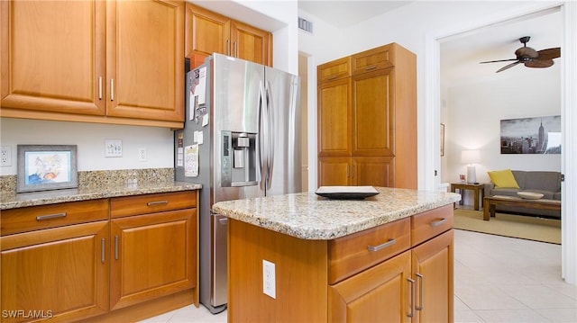 kitchen featuring ceiling fan, stainless steel fridge, light stone counters, and light tile patterned floors