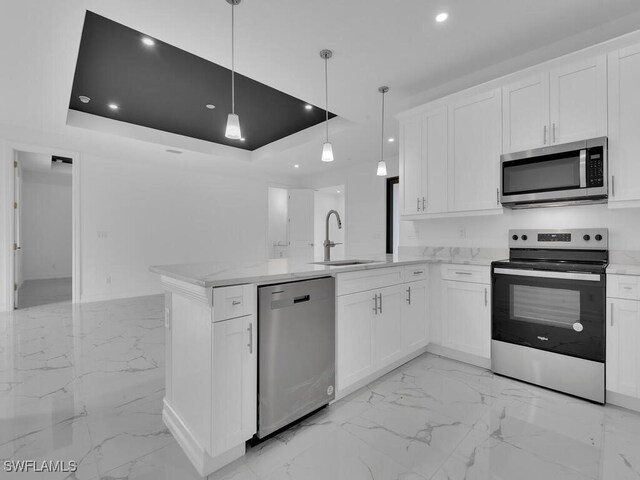 kitchen featuring a tray ceiling, appliances with stainless steel finishes, a peninsula, marble finish floor, and a sink